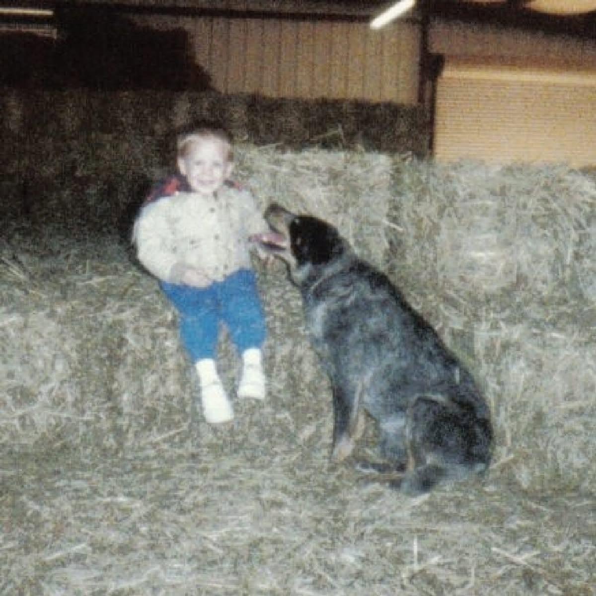 A young Jeremy Farley sitting beside a dog in a barn
